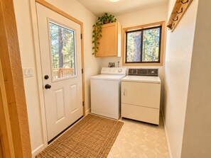A laundry room with a washing machine, dryer, and a window with a view of trees. - Family Cabin Near Murphys | Lake, Hiking & Stargazing (Arnold)