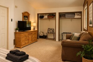 A cozy living room with a television, a wooden cabinet, a sofa, and a chair. There is a closet with shelves and a door. - Family Cabin Near Murphys | Lake, Hiking & Stargazing (Arnold)