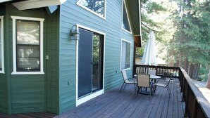 Un edificio verde con una terrazza in legno, una porta scorrevole in vetro e un tavolo con sedie.
