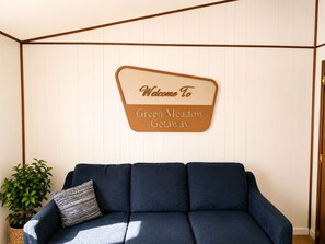A blue sofa with a cushion, a potted plant, and a welcome sign on the wall.