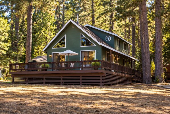A two-story cabin with a deck, surrounded by tall trees.