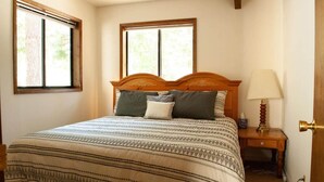 Una camera da letto con un letto, due finestre, un comodino con una lampada e una porta.
