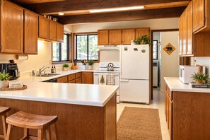 A modern kitchen with wooden cabinets, a central island, and a bear crossing sign on the wall. - Family Cabin Near Murphys | Lake, Hiking & Stargazing (Arnold)