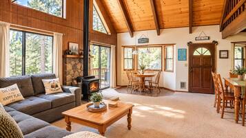 Interior de una cabaña con chimenea, muebles de madera y ventanas amplias.