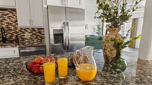 Een keuken met granieten aanrecht, een roestvrijstalen koelkast, een fruitschaal en een karaf sinaasappelsap.