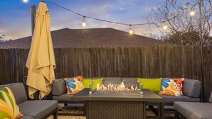 Een terras buiten met een vuurplaats, lichtjes en een houten omheining.