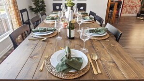Een houten eettafel gedekt met groene servetten, borden en bestek, omringd door stoelen.