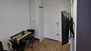 A small, well-lit room with a dining table, chairs, a sofa, and a TV mounted on the wall. - Studio in Champigny sur marne near Disneyland (Champigny-sur-Marne)