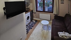 A compact living space with a flat-screen TV, a washing machine, a small table, and a couch. - Studio in Champigny sur marne near Disneyland (Champigny-sur-Marne)
