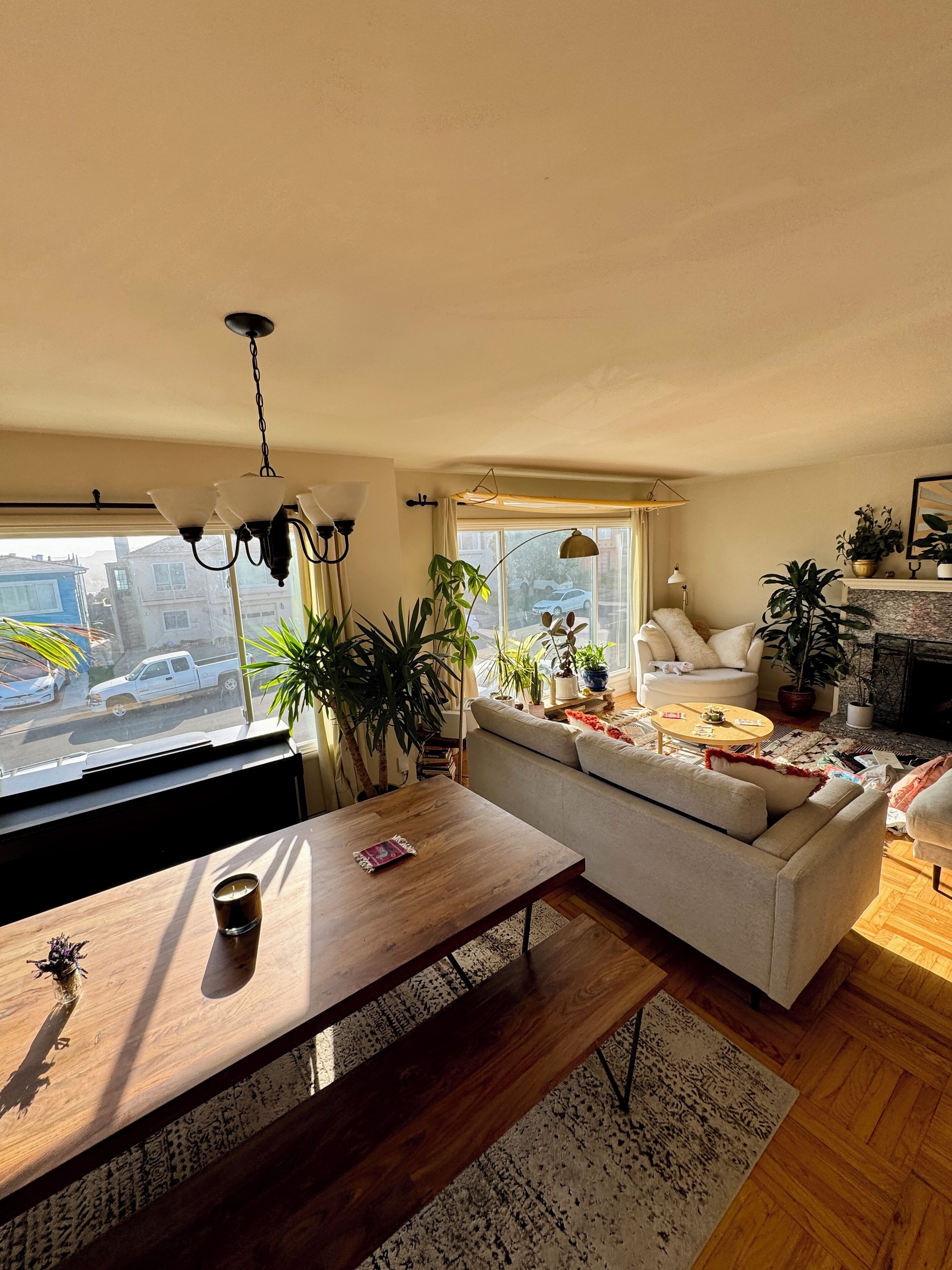 A cozy living room with a sofa, a coffee table, and a dining table. There are plants and a fireplace.