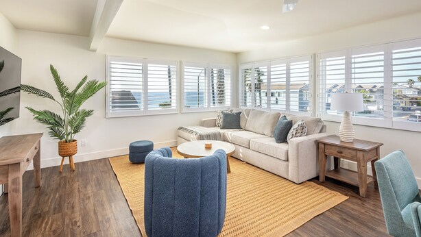 Ein modernes Wohnzimmer mit einer Couch, zwei Sesseln, einem Couchtisch, einem Fernseher und einem Deckenventilator.