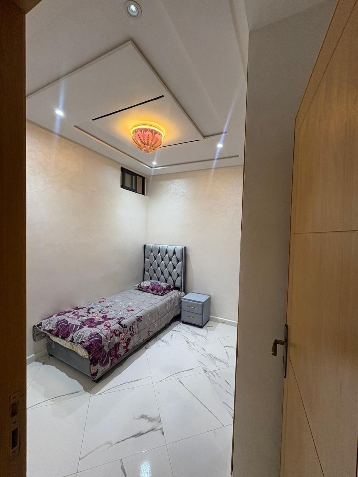 A bedroom with a bed, nightstand, and a ceiling light fixture.