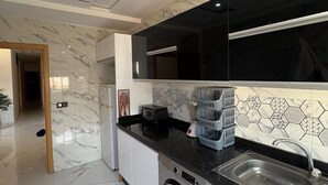 A modern kitchen with a marble backsplash, a built-in washing machine, and a black countertop. - Gulf Serenity Suites (Fès)