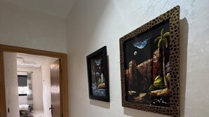 A hallway with two framed artworks on the wall, a wooden door, and a view into another room. - Gulf Serenity Suites (Fès)