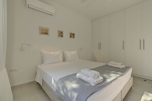 Une chambre à coucher avec un lit, des murs blancs, une armoire et des œuvres d’art.