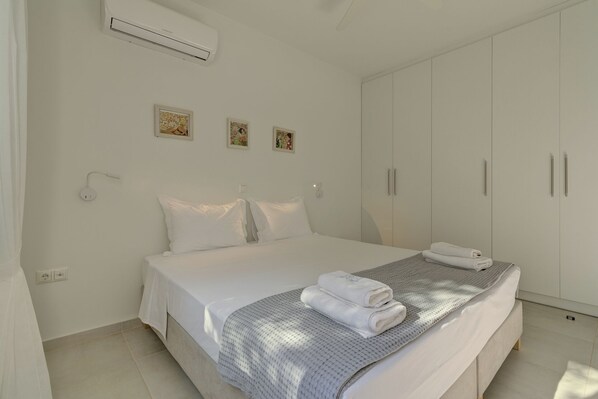 A bedroom with a bed, white walls, a wardrobe, and artwork.