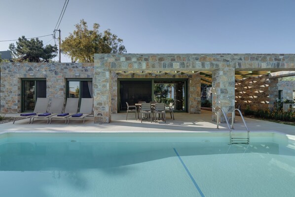A poolside area with lounge chairs and a dining table, stone walls, and a clear pool.