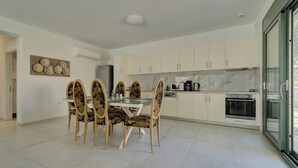 Cuina moderna amb armaris blancs, taula de dinar amb caires florals i una finestra gran.
