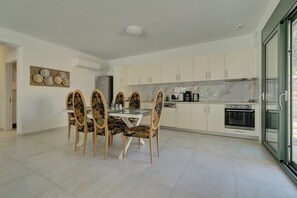 A modern kitchen with white cabinets, a dining table with floral chairs, and a large window. - Ouzo Stone House2 with Private Pool and Parking (Plomari)