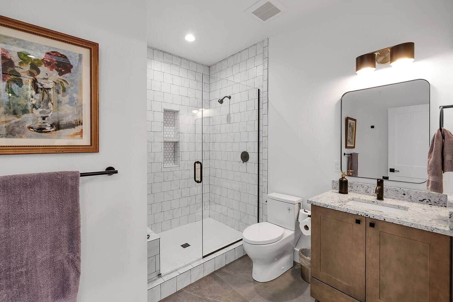 A modern bathroom with a glass-enclosed shower, a toilet, and a vanity with a mirror.
