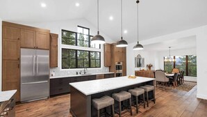 Une cuisine moderne dotée d’un grand îlot central, de meubles en bois, d’appareils électroménagers en acier inoxydable et d’un coin repas offrant une vue agréable.