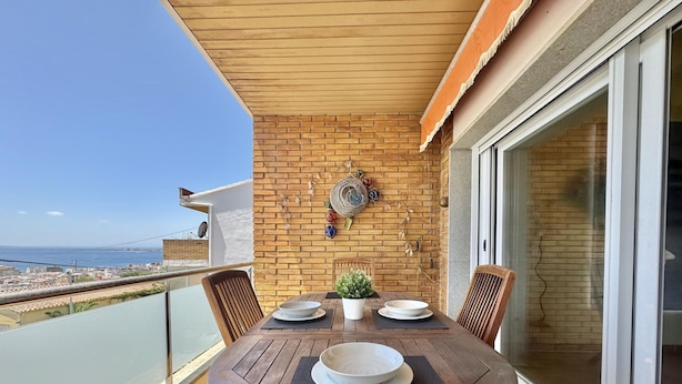 Ein Holztisch mit vier Stühlen auf einem Balkon mit Meerblick.