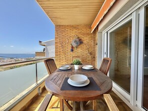 Een houten tafel met vier stoelen op een balkon met uitzicht op zee.