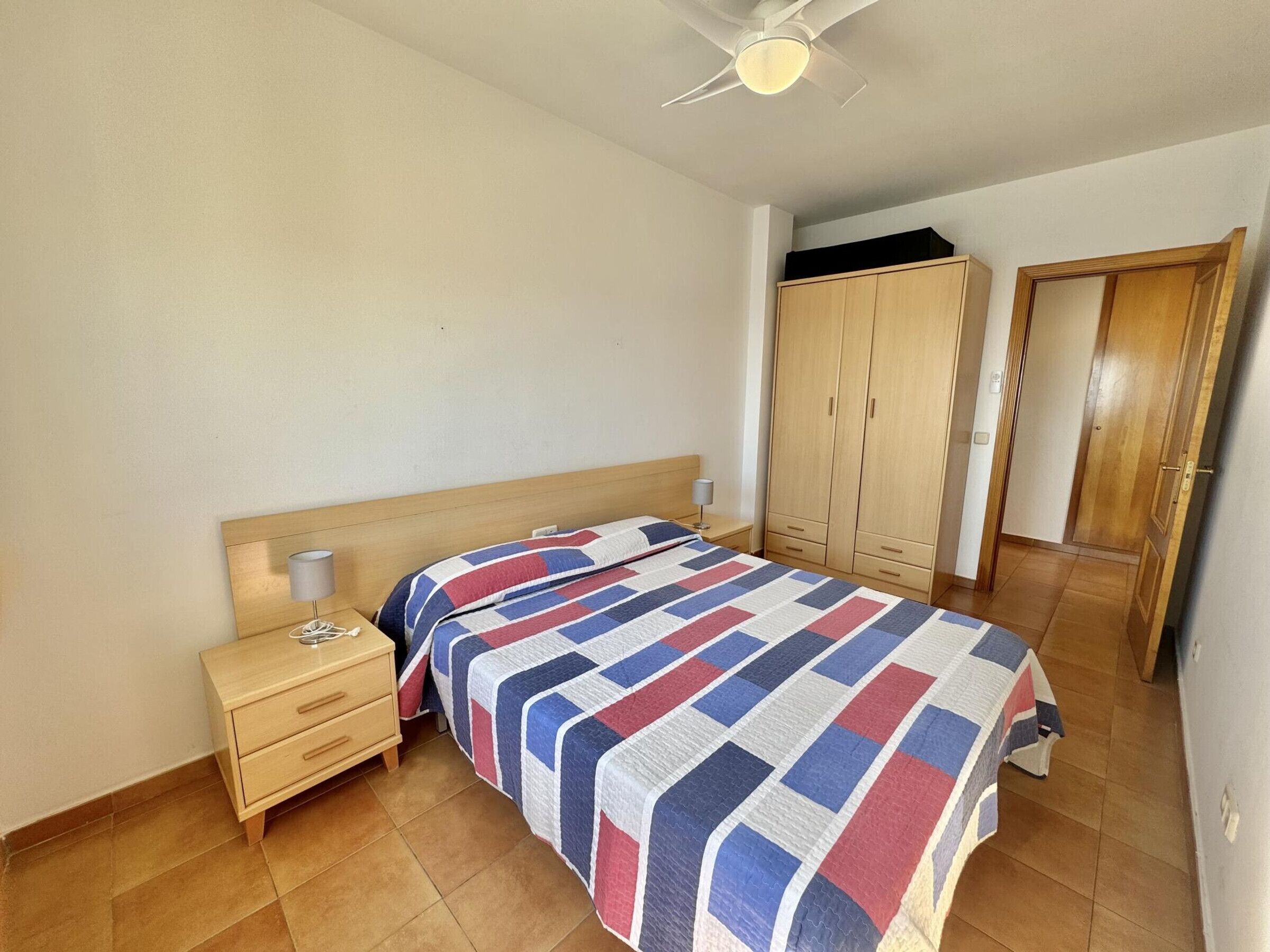 Een slaapkamer met een bed, nachtkastje, kledingkast en plafondventilator.