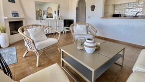 A living room with wicker furniture, a fireplace, a kitchen area, and a dining table. - Apartment in Roses with terrace, private parking, and equipped kitchen (Roses)