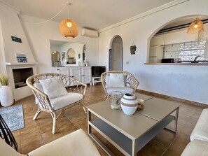Ein Wohnzimmer mit Korbmöbeln, einem Kamin, einer Küchenzeile und einem Esstisch.