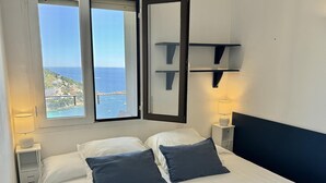 A hotel room with a bed, two bedside lamps, a nightstand, a mirror, and a window with a view of the sea. - Apartment in Roses with terrace, private parking, and equipped kitchen (Roses)