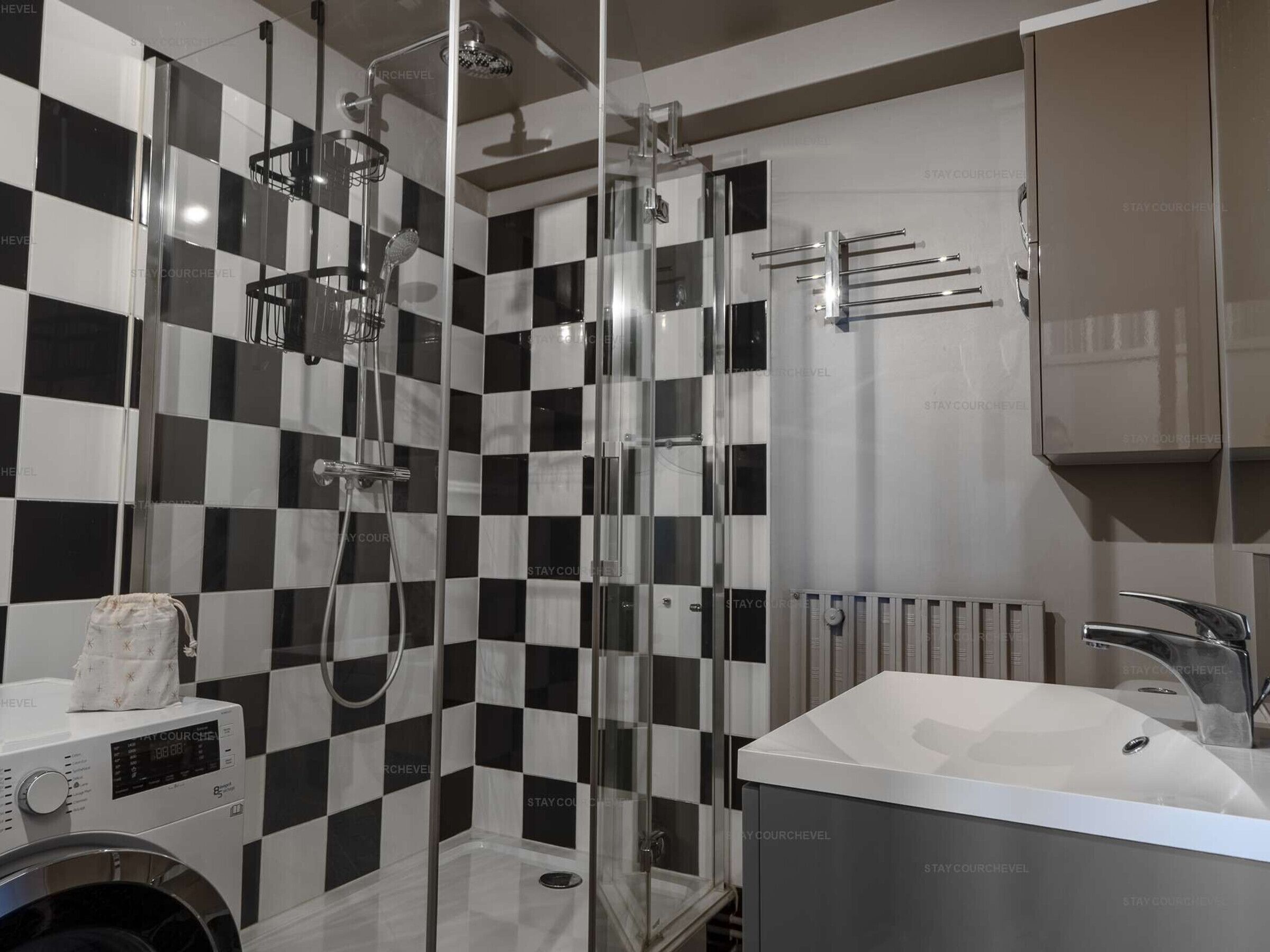 Une salle de bain moderne avec un mur recouvert de carreaux noirs et blancs formant un motif à carreaux, une douche en verre, un lavabo blanc et un porte-serviettes.