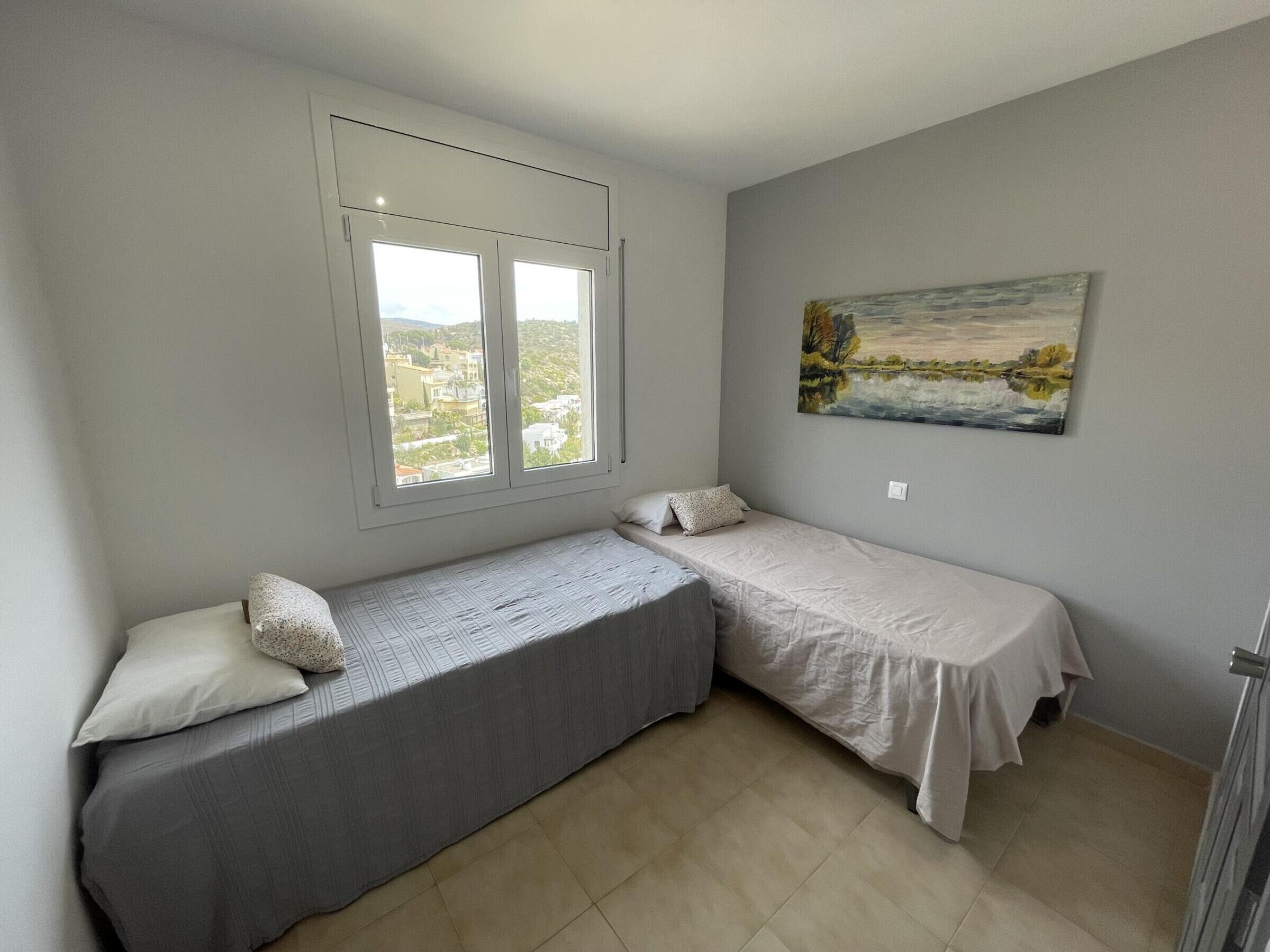 Une petite chambre avec deux lits simples, une fenêtre donnant sur un beau paysage et un tableau accroché au mur.
