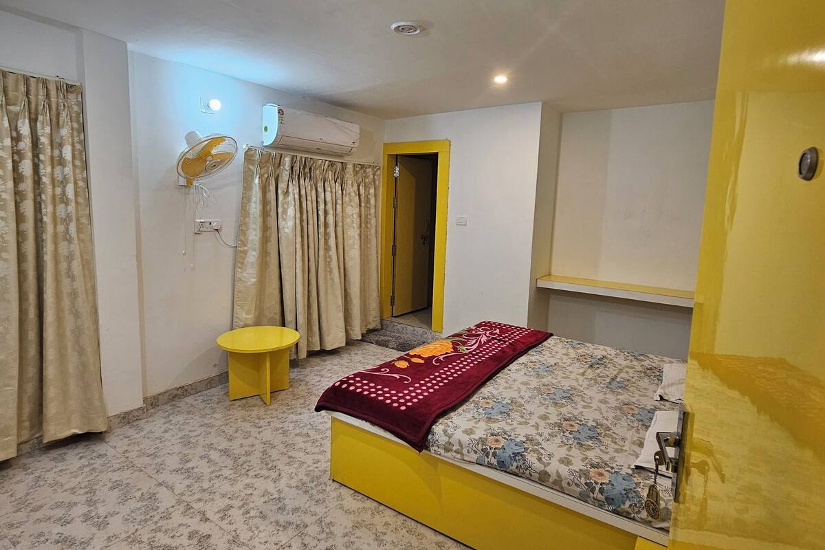 A bedroom with a bed, curtains, an air conditioning unit, and a small table.