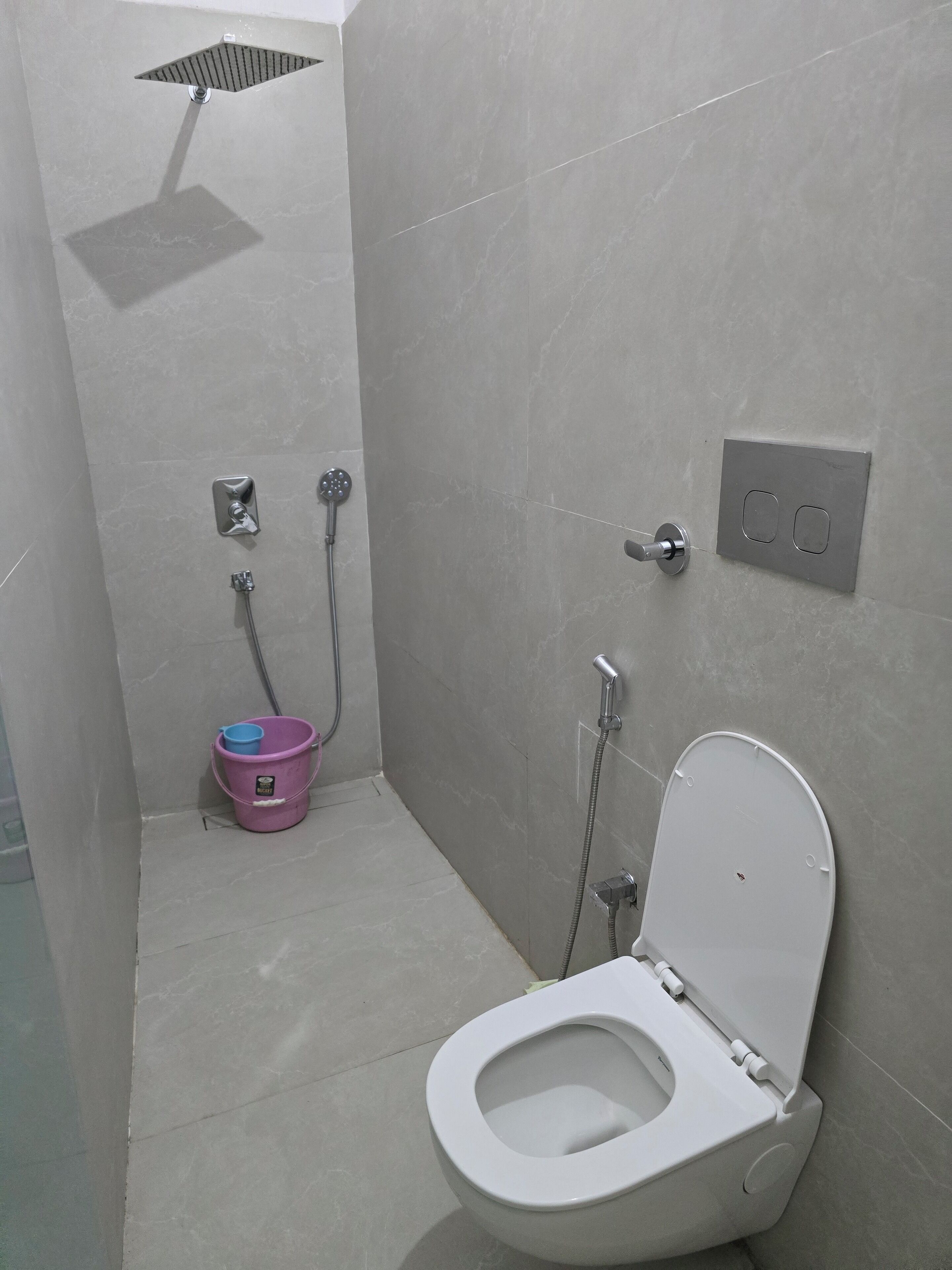A small, modern bathroom with a toilet, a shower, and a bucket.