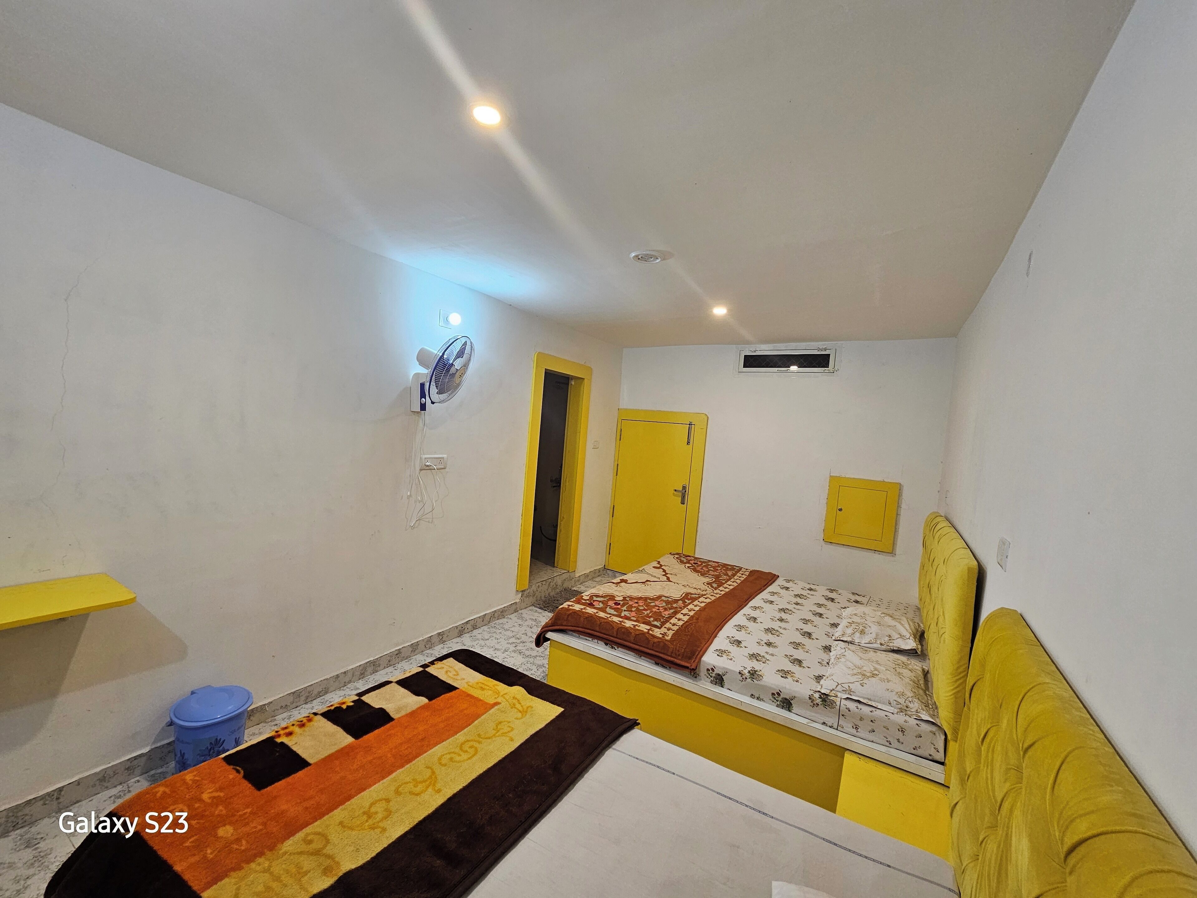 A bedroom with a bed, a fan, a door, and a small window.