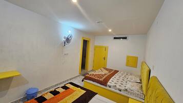 A bedroom with a bed, a fan, a door, and a small window.
