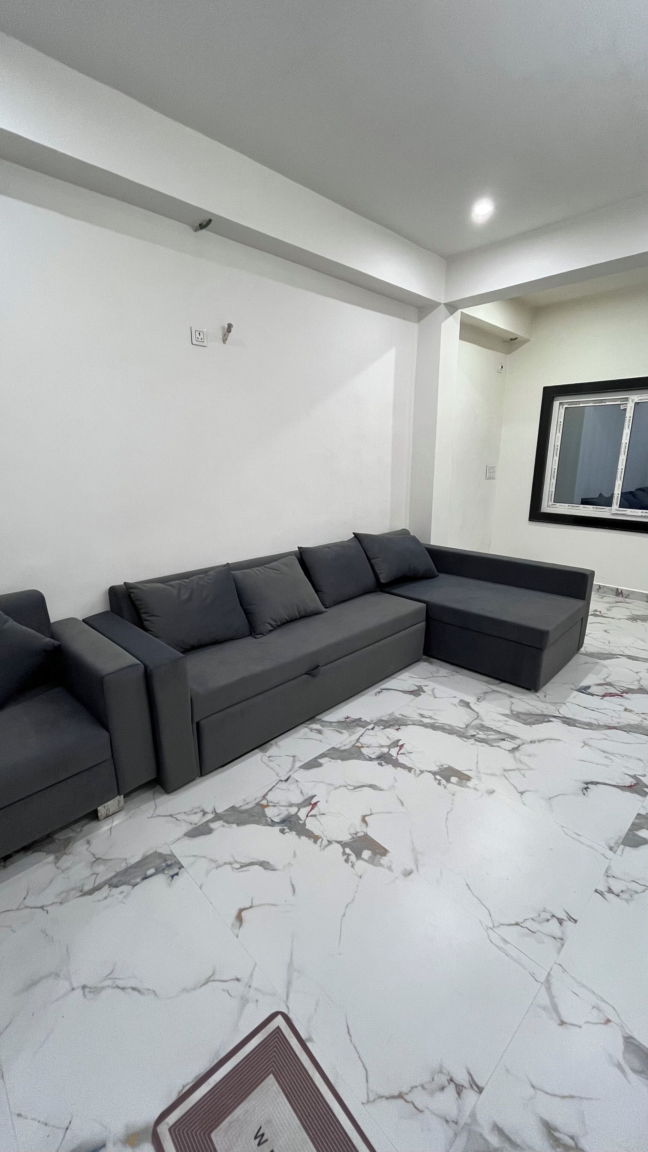 A modern living room with a sectional sofa, a marble-patterned floor, and a large window.