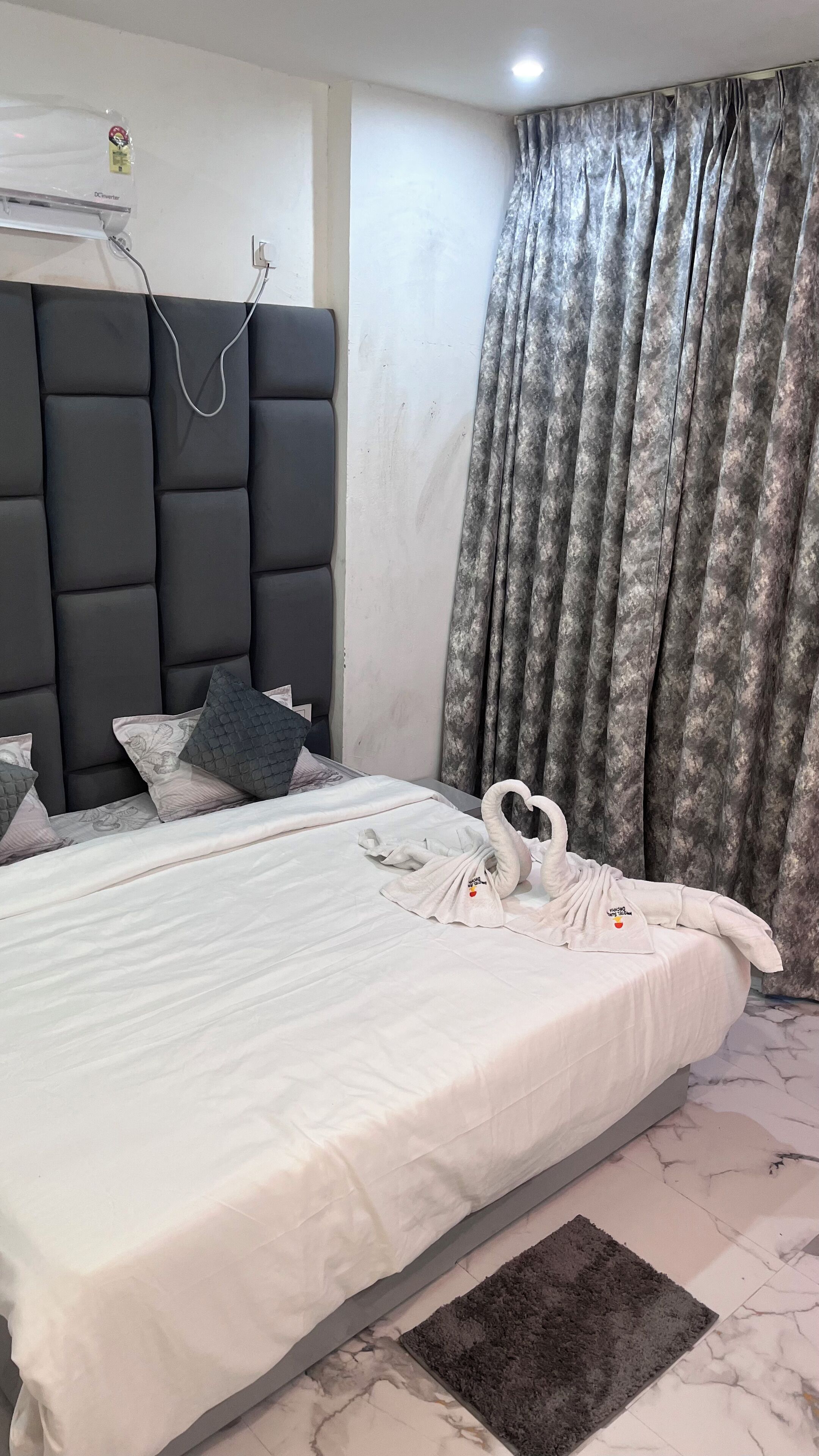 A neatly made bed with a white comforter and pillows, a dark headboard, and a grey curtain.