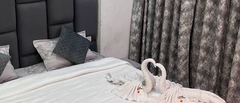 A neatly made bed with a white comforter and pillows, a dark headboard, and a grey curtain.
