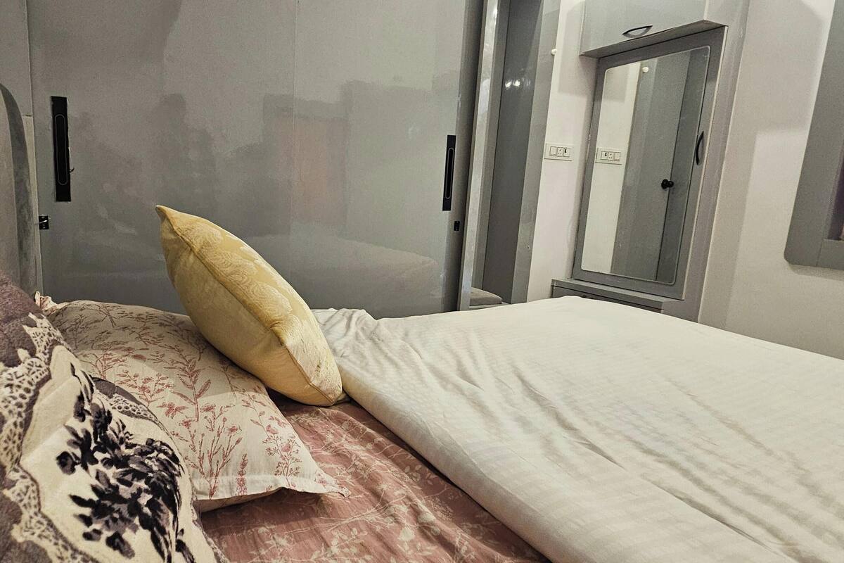 A hotel room with a bed, a bedside table, a mirror, and a window with curtains.