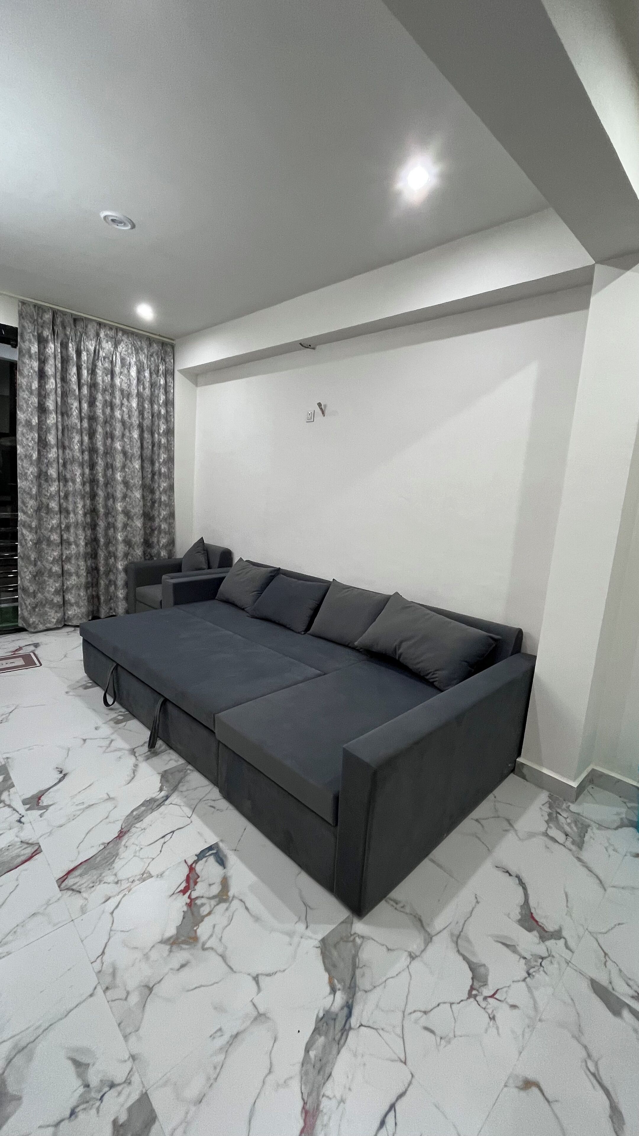 Ein modernes Wohnzimmer mit einem dunkelgrauen Sofa, einem kleinen Beistelltisch und einem Boden mit Marmoroptik.