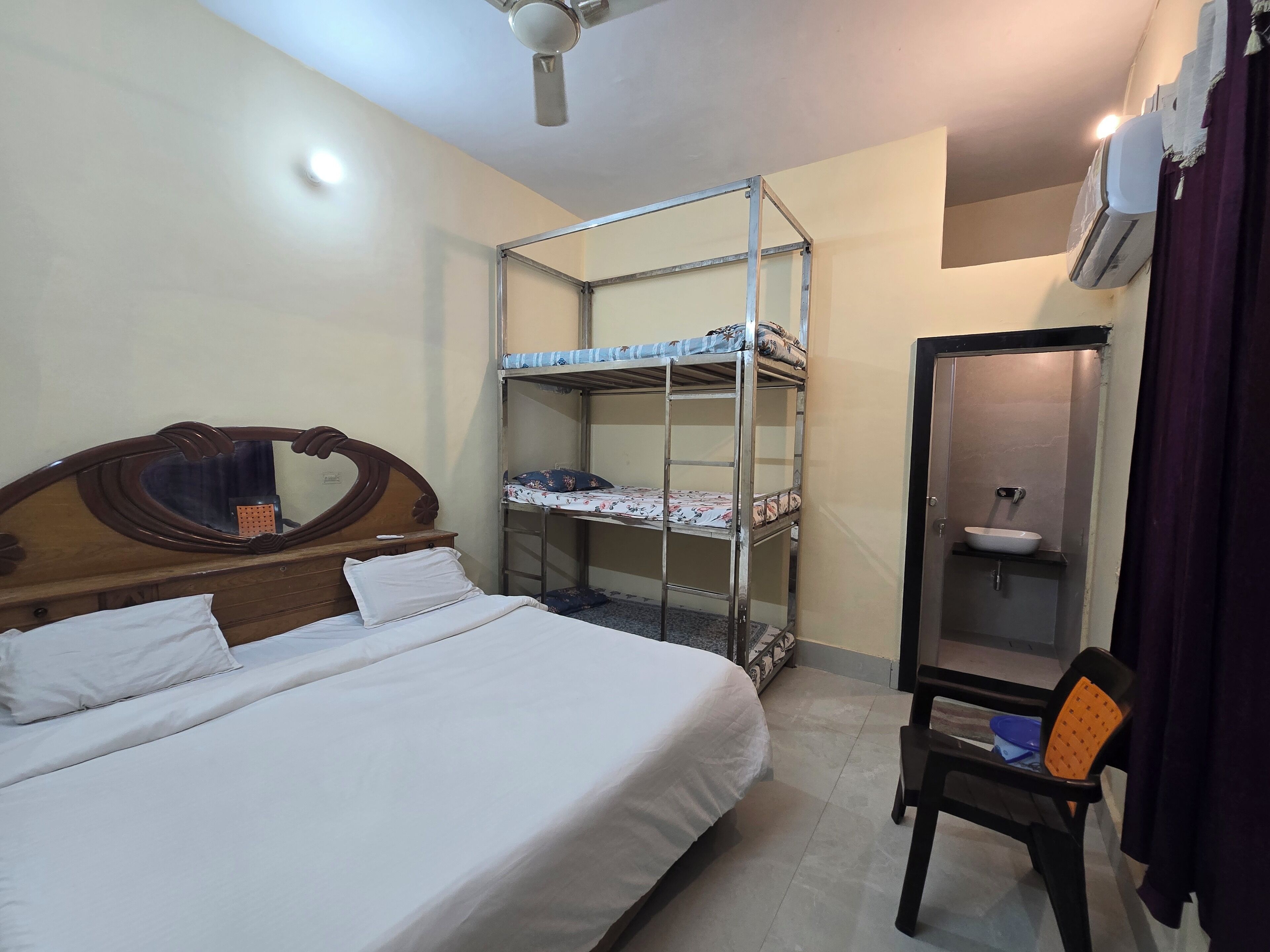 A bedroom with a bunk bed, a wooden headboard, a mirror, a small table, a chair, and a bathroom with a sink and mirror.