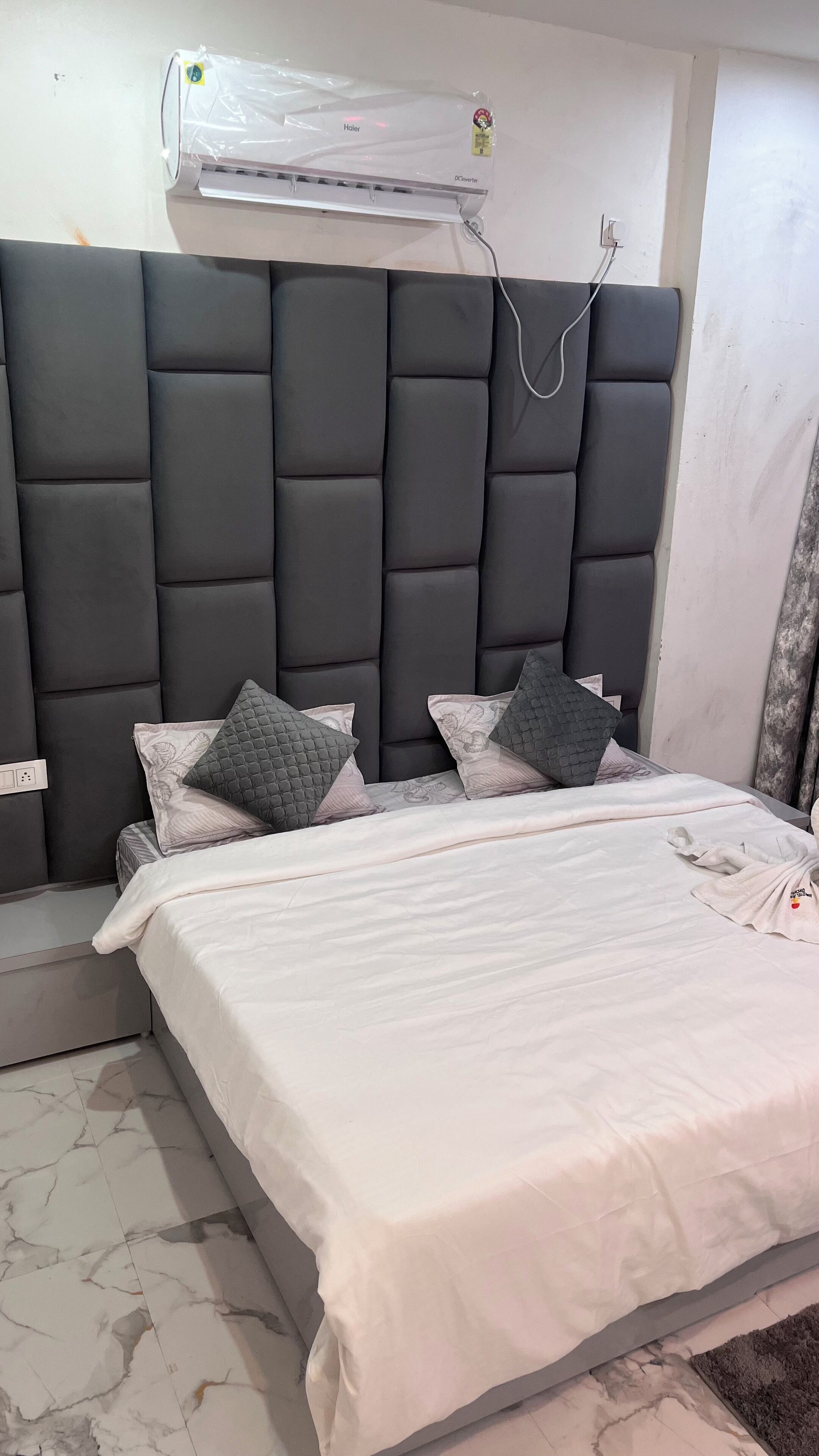 A bedroom with a dark upholstered headboard, a bed with white linens, and a wall-mounted air conditioner.