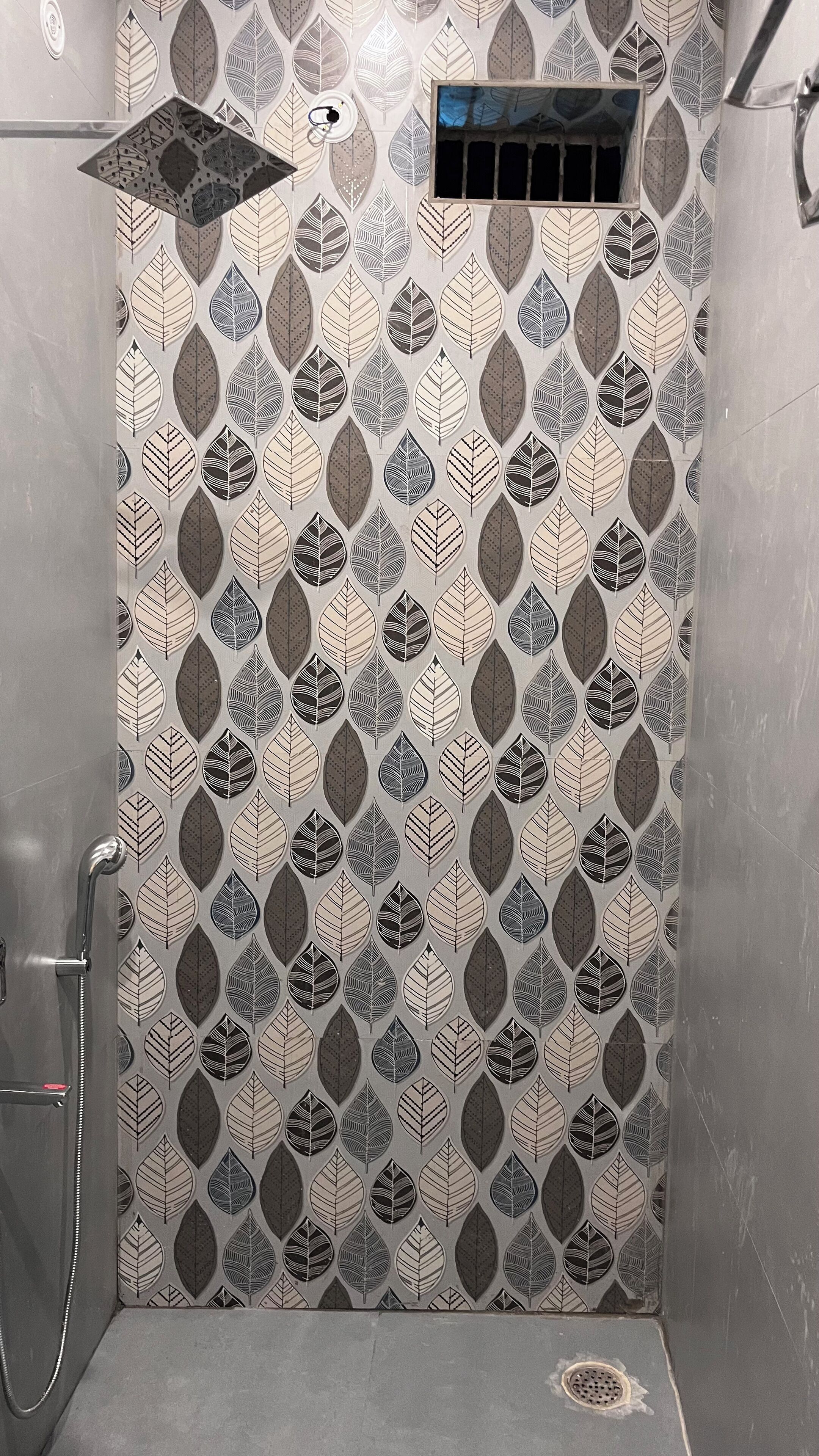 Zona de ducha con pared de azulejos estampados, un cabezal de ducha y una ventana pequeña.