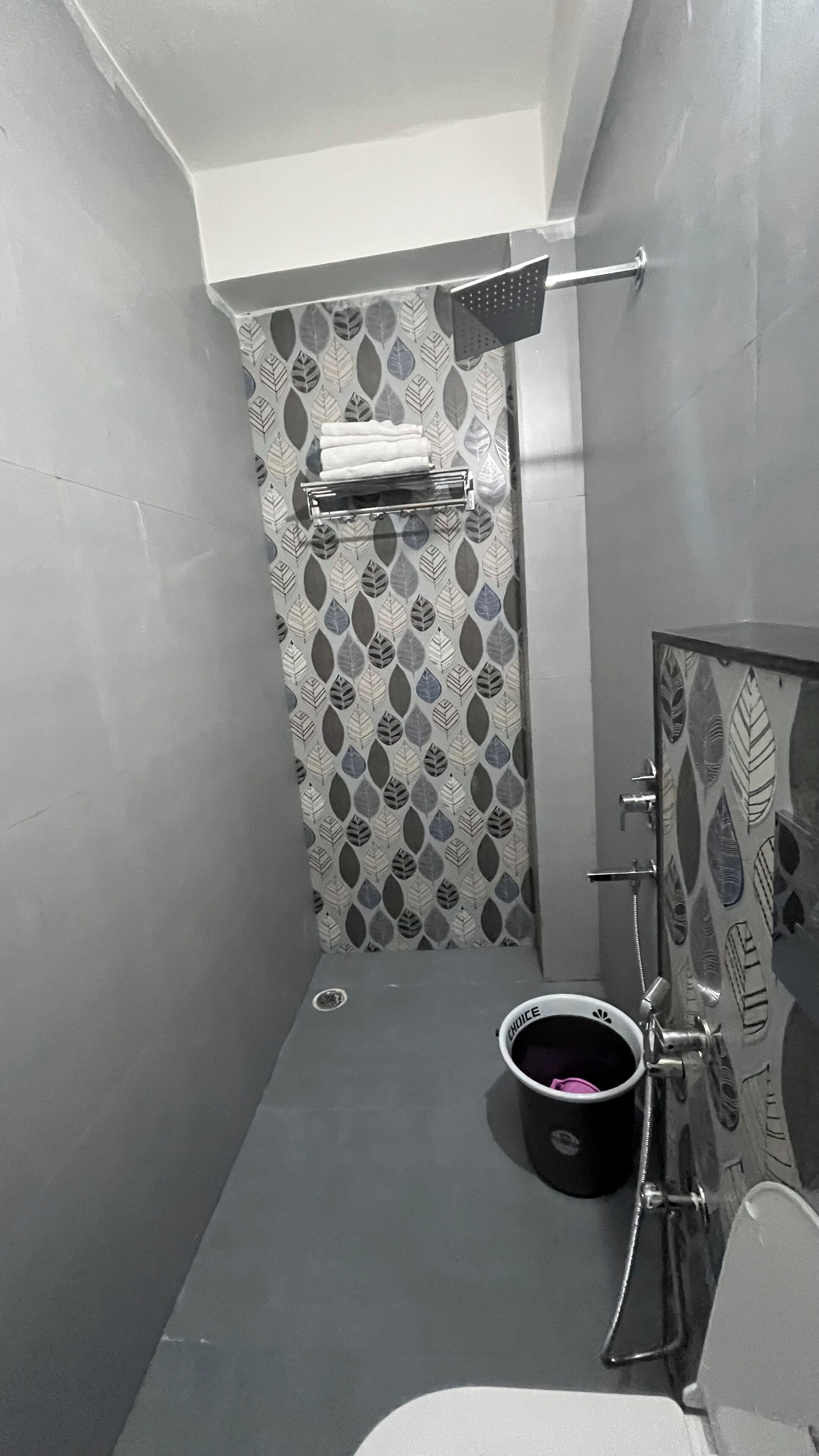 Un baño pequeño con ducha, perchero y un cubo.