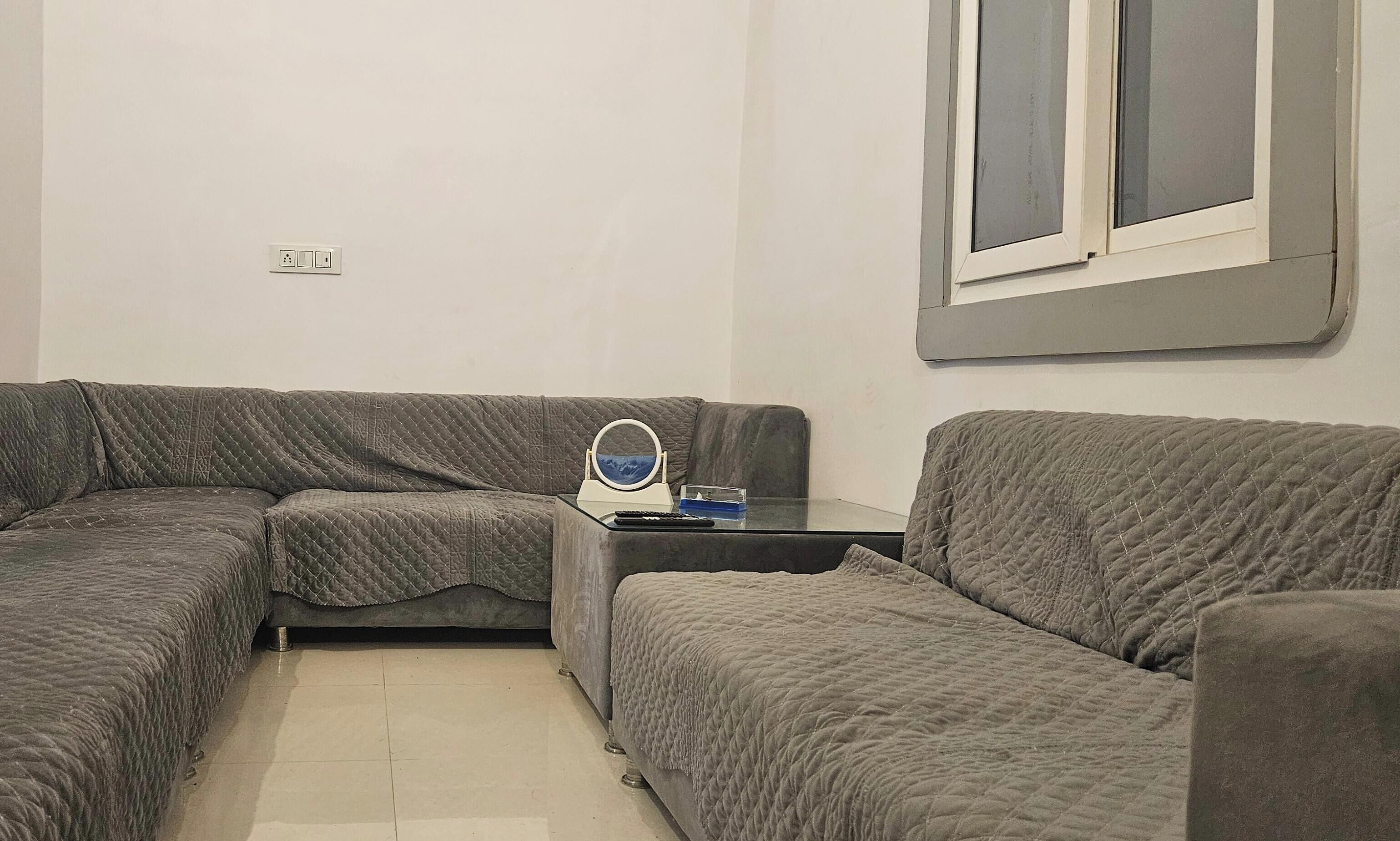 A living room with a grey sectional sofa, a small glass coffee table, and a ring light.