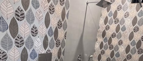 Un baño con un diseño de hojas estampado en las paredes, un inodoro blanco, una zona de ducha y un lavabo con lavamanos negro.