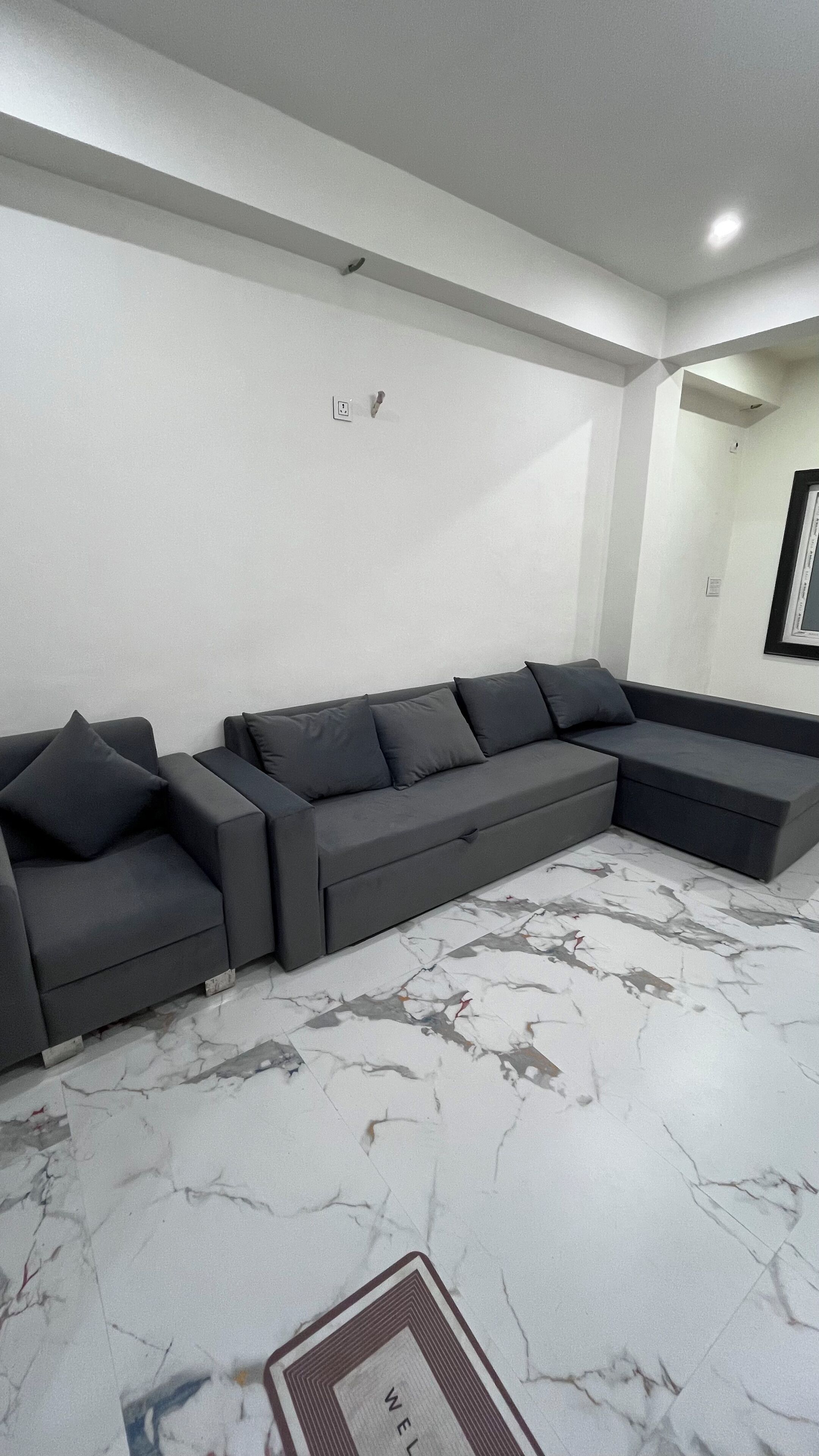 Ein modernes Wohnzimmer mit einem Ecksofa, einem Boden mit Marmormuster und einem gerahmten Bild an der Wand.