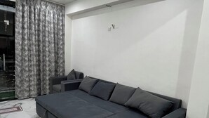 A modern living room with a grey sectional sofa, a marble-patterned floor, and a large window with grey curtains. - Hotel Sunset Orchha (Orchha)